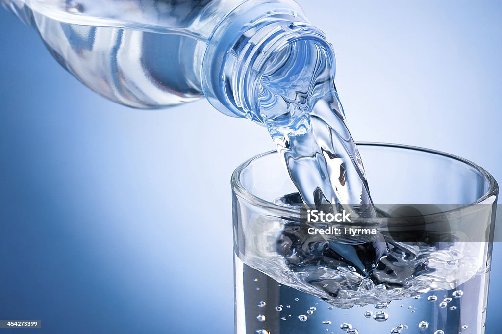 Pouring water from bottle into glass on blue background